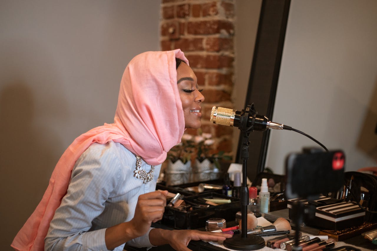 Muslim woman in headscarf prepares beauty vlog with microphone in modern indoor setting.