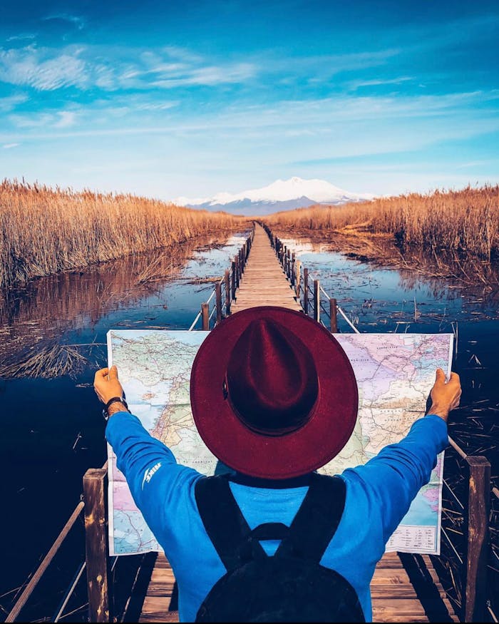 Adventurer with map on a bridge path over a serene water landscape under a clear blue sky.