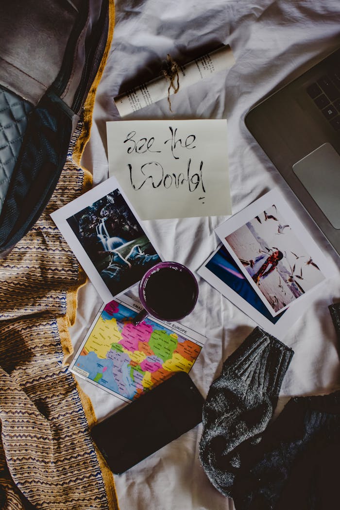 Flat lay of travel planning essentials on a bed, including photos, map, and a laptop.